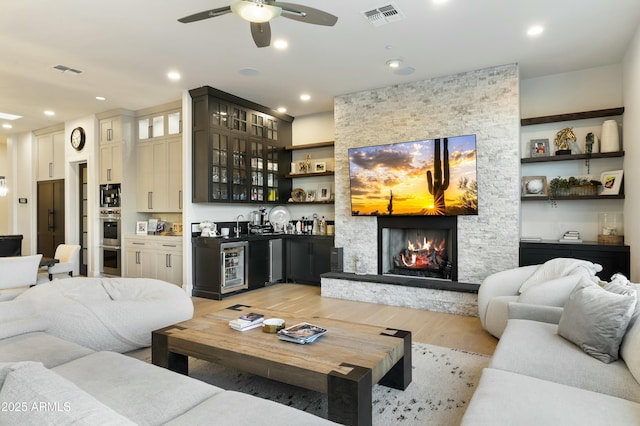 living room featuring bar, light hardwood / wood-style floors, ceiling fan, wine cooler, and a fireplace