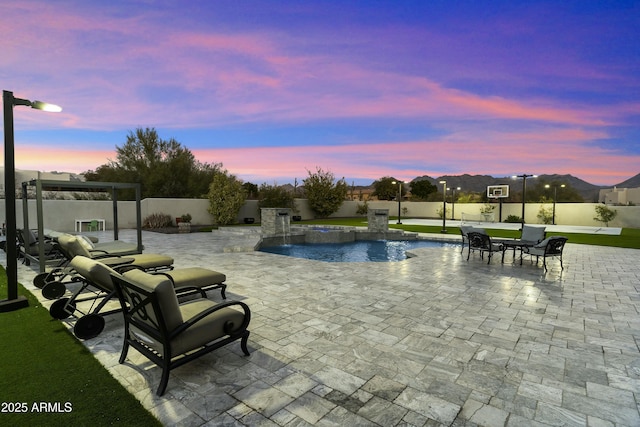 pool at dusk with pool water feature and a patio