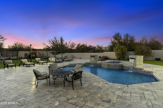 pool at dusk featuring an in ground hot tub, a playground, pool water feature, and a patio