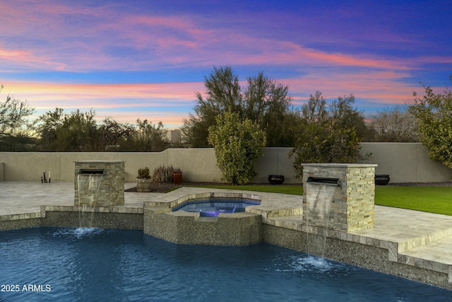 pool at dusk with pool water feature, a patio area, and an in ground hot tub