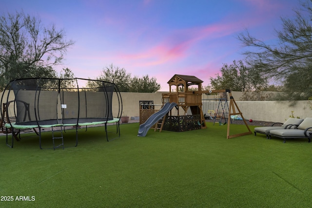 playground at dusk featuring a trampoline and a yard