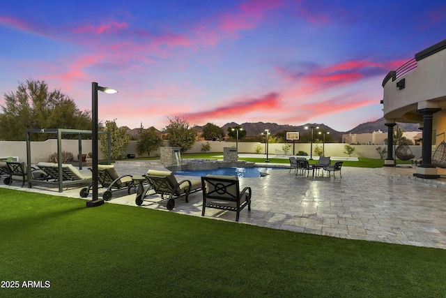 pool at dusk with pool water feature, a yard, a pergola, and a patio