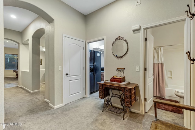 hall with arched walkways, baseboards, and light colored carpet