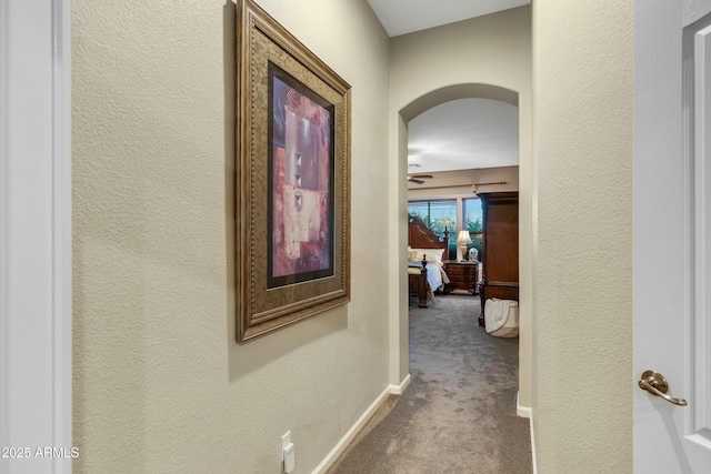 hallway with carpet, arched walkways, baseboards, and a textured wall