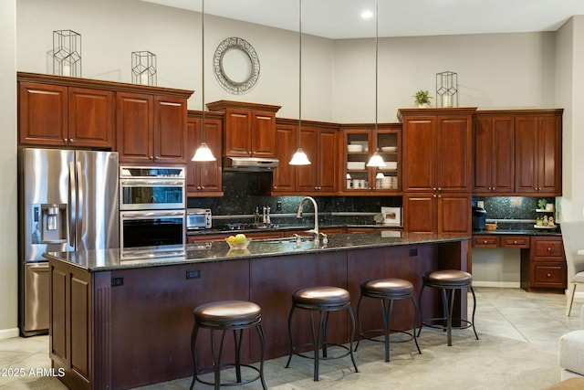 kitchen with a breakfast bar, a towering ceiling, appliances with stainless steel finishes, light tile patterned flooring, and under cabinet range hood