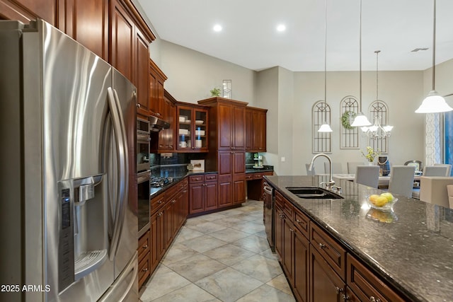 kitchen featuring decorative light fixtures, stainless steel appliances, glass insert cabinets, a sink, and dark stone counters