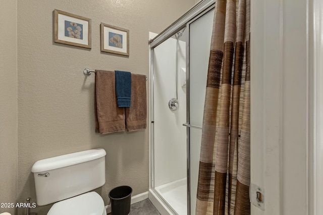 bathroom featuring baseboards, a textured wall, a shower stall, and toilet