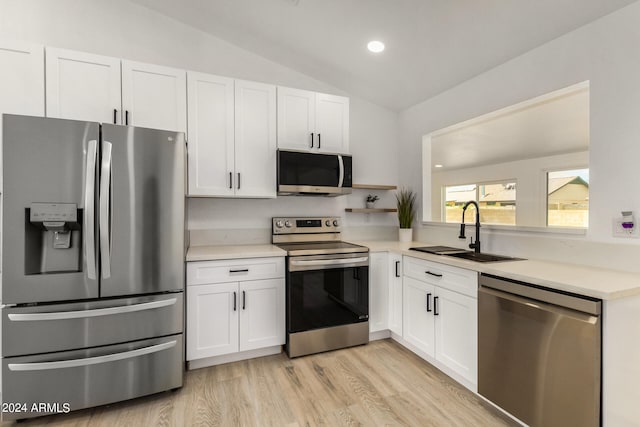 kitchen with vaulted ceiling, sink, stainless steel appliances, and white cabinetry