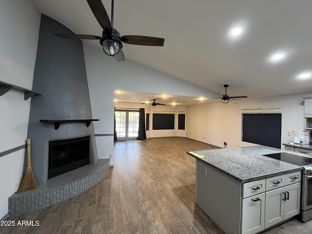 kitchen featuring light stone counters, a brick fireplace, ceiling fan, stainless steel electric stove, and light hardwood / wood-style floors