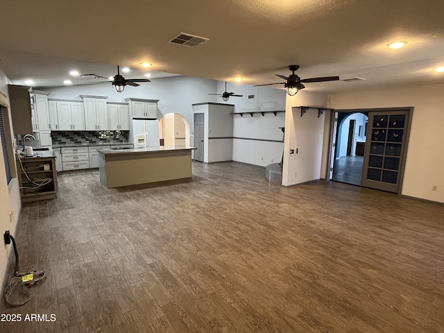 kitchen with a kitchen island, tasteful backsplash, white cabinets, dark hardwood / wood-style flooring, and white fridge with ice dispenser