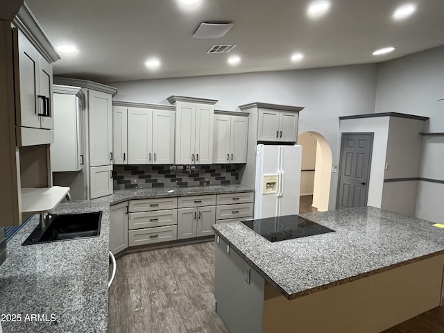 kitchen with light stone counters, black electric stovetop, white refrigerator with ice dispenser, and hardwood / wood-style floors