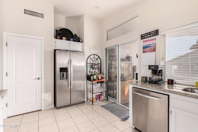 kitchen with light stone counters, stainless steel appliances, white cabinets, and light tile patterned flooring