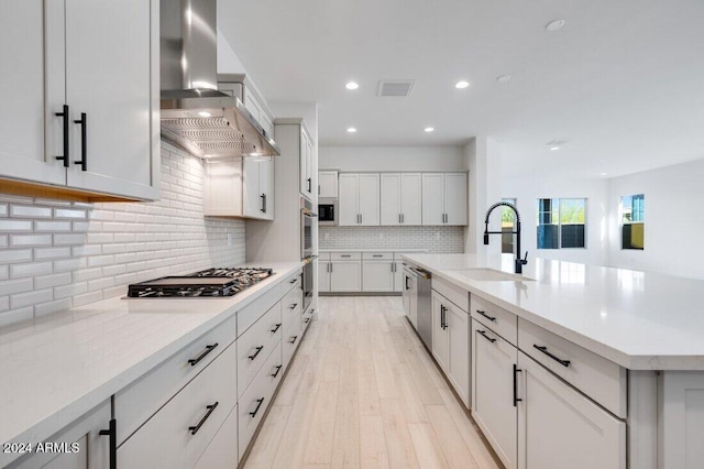 kitchen with a large island with sink, sink, light hardwood / wood-style flooring, wall chimney exhaust hood, and stainless steel appliances