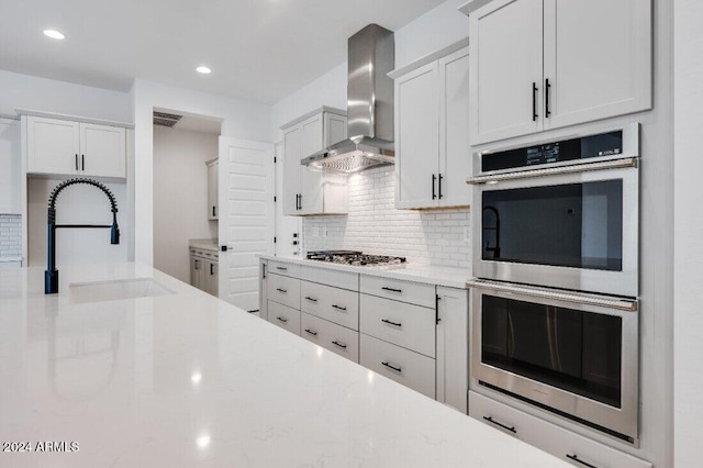 kitchen with white cabinetry, sink, light stone countertops, wall chimney range hood, and appliances with stainless steel finishes