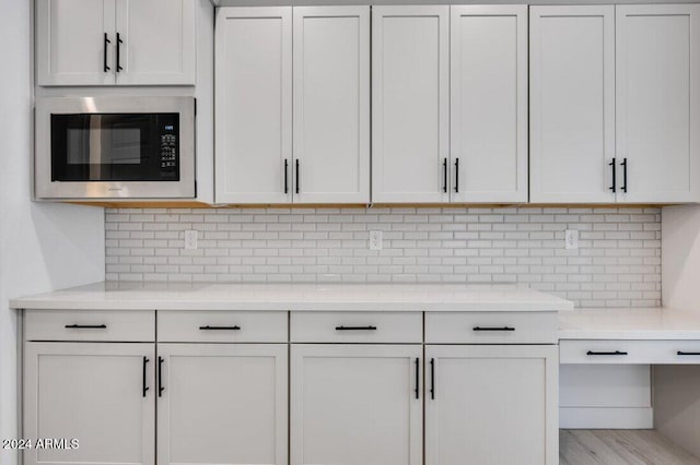 kitchen featuring tasteful backsplash, light hardwood / wood-style flooring, white cabinetry, and stainless steel microwave