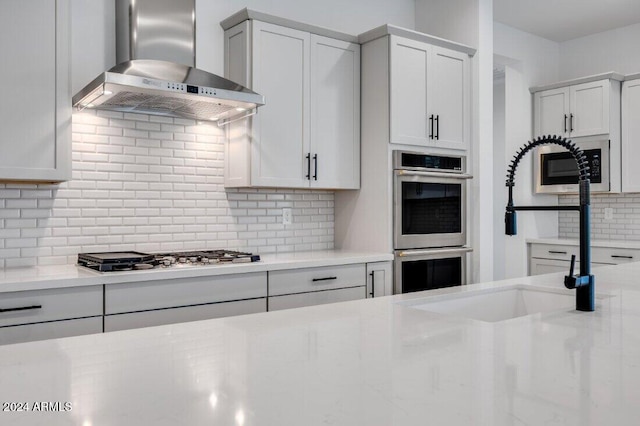 kitchen with sink, wall chimney exhaust hood, appliances with stainless steel finishes, tasteful backsplash, and white cabinetry