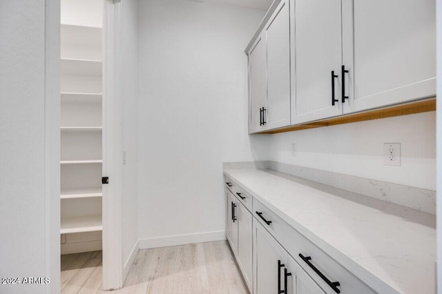 bar featuring white cabinets, light wood-type flooring, and light stone counters