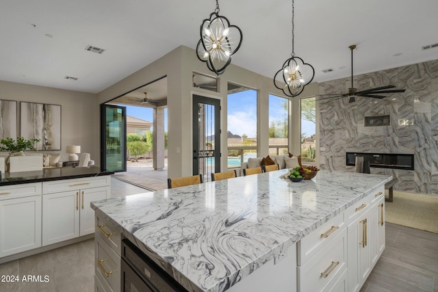 kitchen with ceiling fan with notable chandelier, white cabinets, hanging light fixtures, a kitchen island, and a fireplace