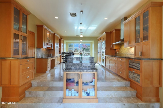 kitchen featuring a center island with sink, wall chimney exhaust hood, hanging light fixtures, and tasteful backsplash