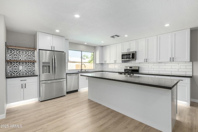 kitchen featuring stainless steel appliances, tasteful backsplash, dark countertops, and light wood-style floors