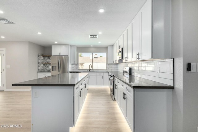 kitchen featuring stainless steel appliances, dark countertops, decorative backsplash, light wood-style floors, and a sink