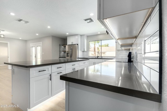 kitchen with visible vents, stainless steel fridge with ice dispenser, dark countertops, light wood-style flooring, and a sink