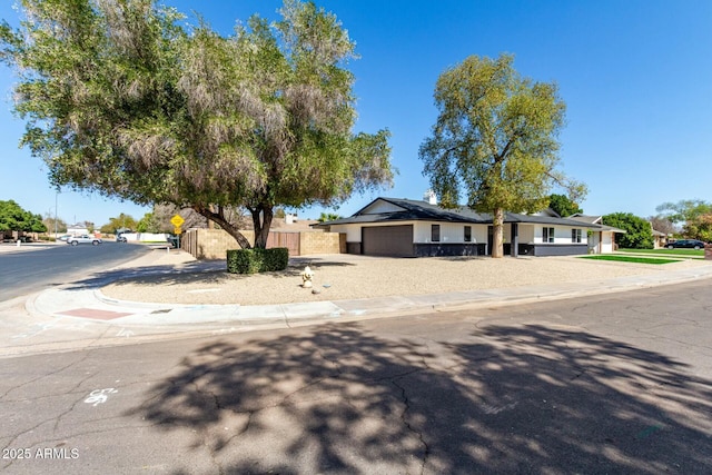 view of front of house featuring solar panels, driveway, an attached garage, and fence