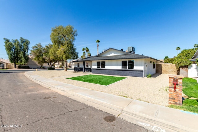 view of front of house featuring brick siding, fence, central AC, and a front lawn