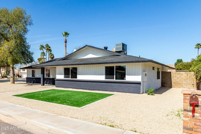 view of front of home with roof with shingles, central AC, brick siding, and fence