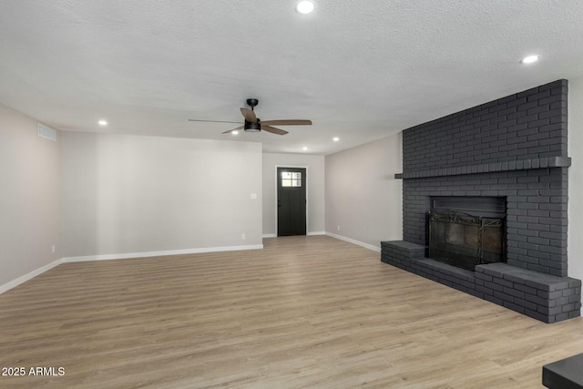 unfurnished living room with a fireplace, a ceiling fan, a textured ceiling, light wood-type flooring, and baseboards