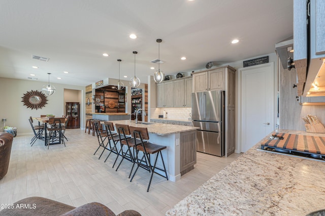kitchen with a sink, freestanding refrigerator, recessed lighting, a kitchen bar, and visible vents