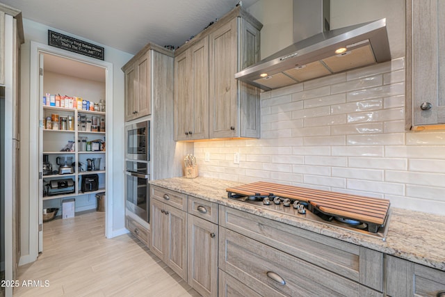 kitchen with wall chimney range hood, appliances with stainless steel finishes, tasteful backsplash, and light stone counters