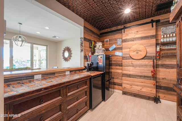 kitchen featuring wooden walls, dark brown cabinetry, recessed lighting, refrigerator, and pendant lighting