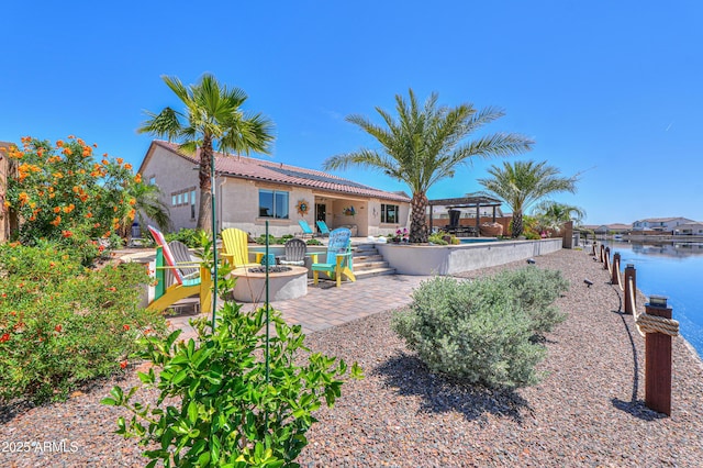 exterior space featuring a water view, a tile roof, a patio, a fire pit, and stucco siding