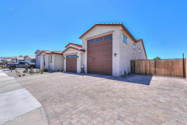 mediterranean / spanish-style house featuring a tiled roof, driveway, a garage, fence, and stucco siding
