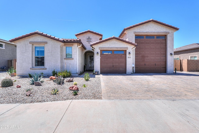 mediterranean / spanish-style house with fence, an attached garage, a tile roof, stucco siding, and decorative driveway