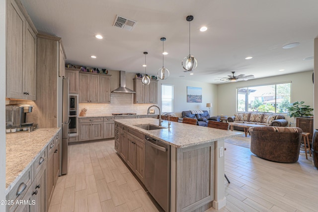 kitchen featuring visible vents, light wood-style floors, wall chimney range hood, a sink, and stainless steel appliances