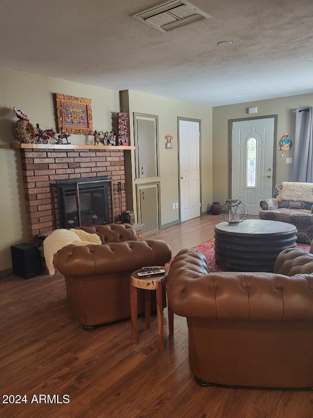 living room with dark hardwood / wood-style flooring, a textured ceiling, and a brick fireplace