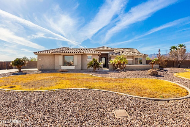 mediterranean / spanish-style home featuring a tile roof, fence, a front lawn, and stucco siding