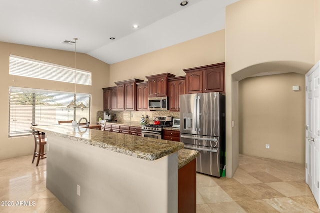 kitchen featuring visible vents, arched walkways, an island with sink, stainless steel appliances, and backsplash