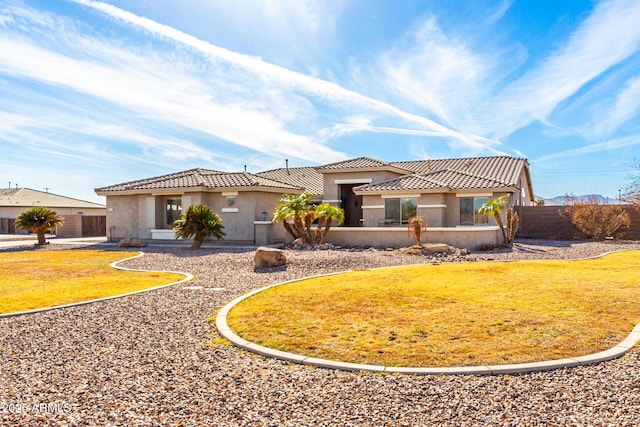 mediterranean / spanish home with a front lawn, a tile roof, fence, and stucco siding