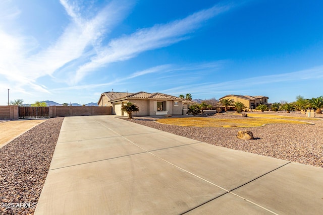 view of front facade with stucco siding, concrete driveway, a gate, fence, and a tiled roof