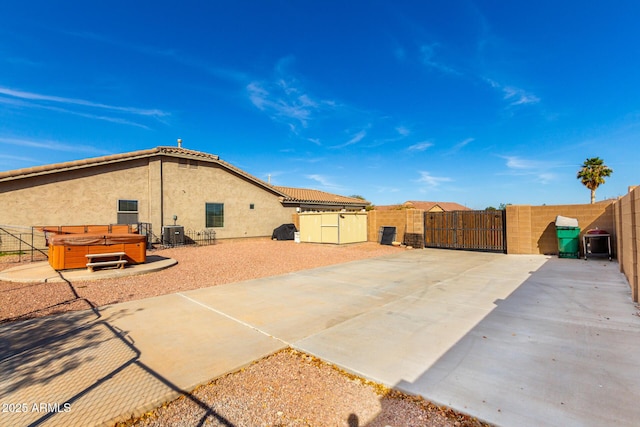back of property with stucco siding, a hot tub, central AC unit, a gate, and fence