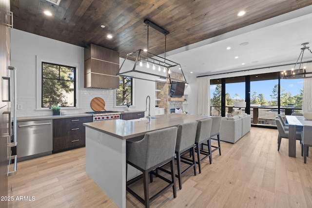 kitchen featuring decorative light fixtures, ventilation hood, an island with sink, a chandelier, and stainless steel appliances