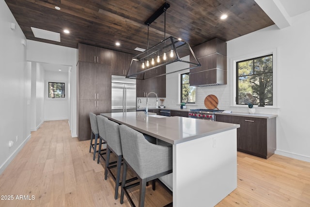 kitchen featuring sink, a center island with sink, premium appliances, custom range hood, and pendant lighting
