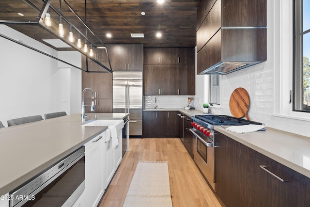 kitchen with premium range hood, a breakfast bar area, high end appliances, hanging light fixtures, and light wood-type flooring