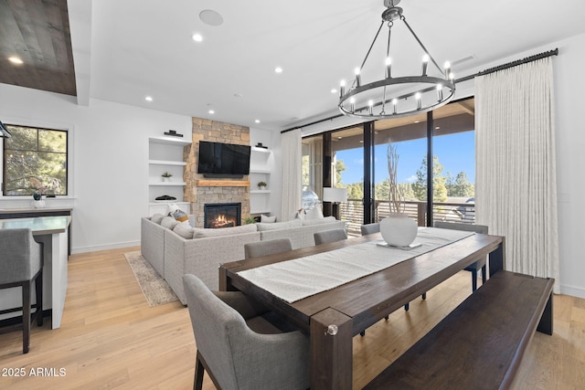 dining area featuring a stone fireplace, light hardwood / wood-style floors, built in shelves, and a chandelier