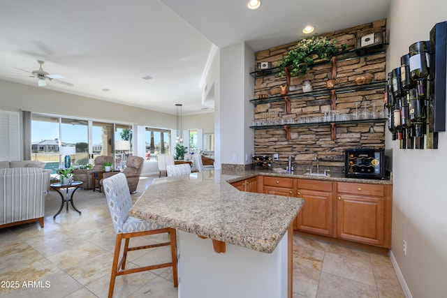 kitchen featuring a kitchen bar, kitchen peninsula, ornamental molding, ceiling fan, and hanging light fixtures