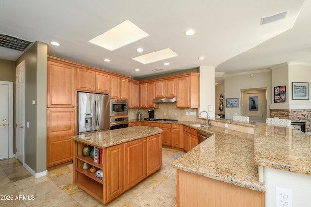 kitchen with sink, a skylight, light stone countertops, appliances with stainless steel finishes, and kitchen peninsula