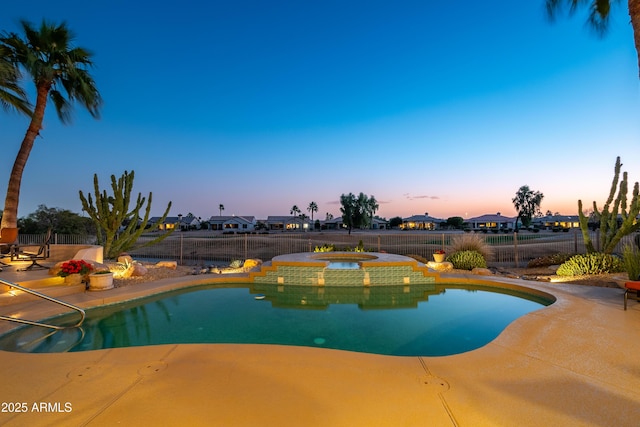 pool at dusk featuring a patio area and an in ground hot tub